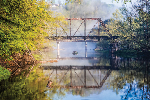 "Fishing Under the Trestle" by Debra and Dave Vanderlaan... A beautiful Spring morning on the river, fog rolling in under the trestle. These fishing buddies, a man and is dog, are cruising around the swollen river on this pretty misty dawn. This is the Valley River where it meets the Hiwassee River just beyond the fog in the convergeance curve in the river. Fresh leaves hang on the branches along the edge of the stream. Sunlight breaks through the cloudy mist to light up the sycamore and willow trees along the banks... Enjoy our big gallery of fine art photography images! Www.CelebrateLifeGallery.com