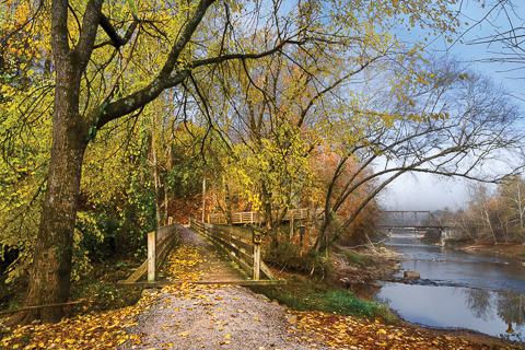 "The Park" by Debra and Dave Vanderlaan... The boardwalk in Konaheeta Park along the Valley River in Murphy, North Carolina is so very pretty especially in the autumn. Shown here on a foggy morning, the beech trees are tumbling and lay like confetti on the warm wood of the walkway. The old trestle can be seen in the distance, an abandoned railway that used to connect the Lexington and Nashville line... This trail is called the River Walk and winds along the river and through the park for nearly 3 miles one way... Enjoy and Share our beautiful Appalachian Blue Ridge mountain images!!